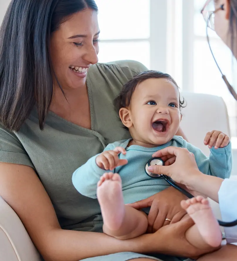 Woman holding her smiling and laughing baby while a doctor examines him